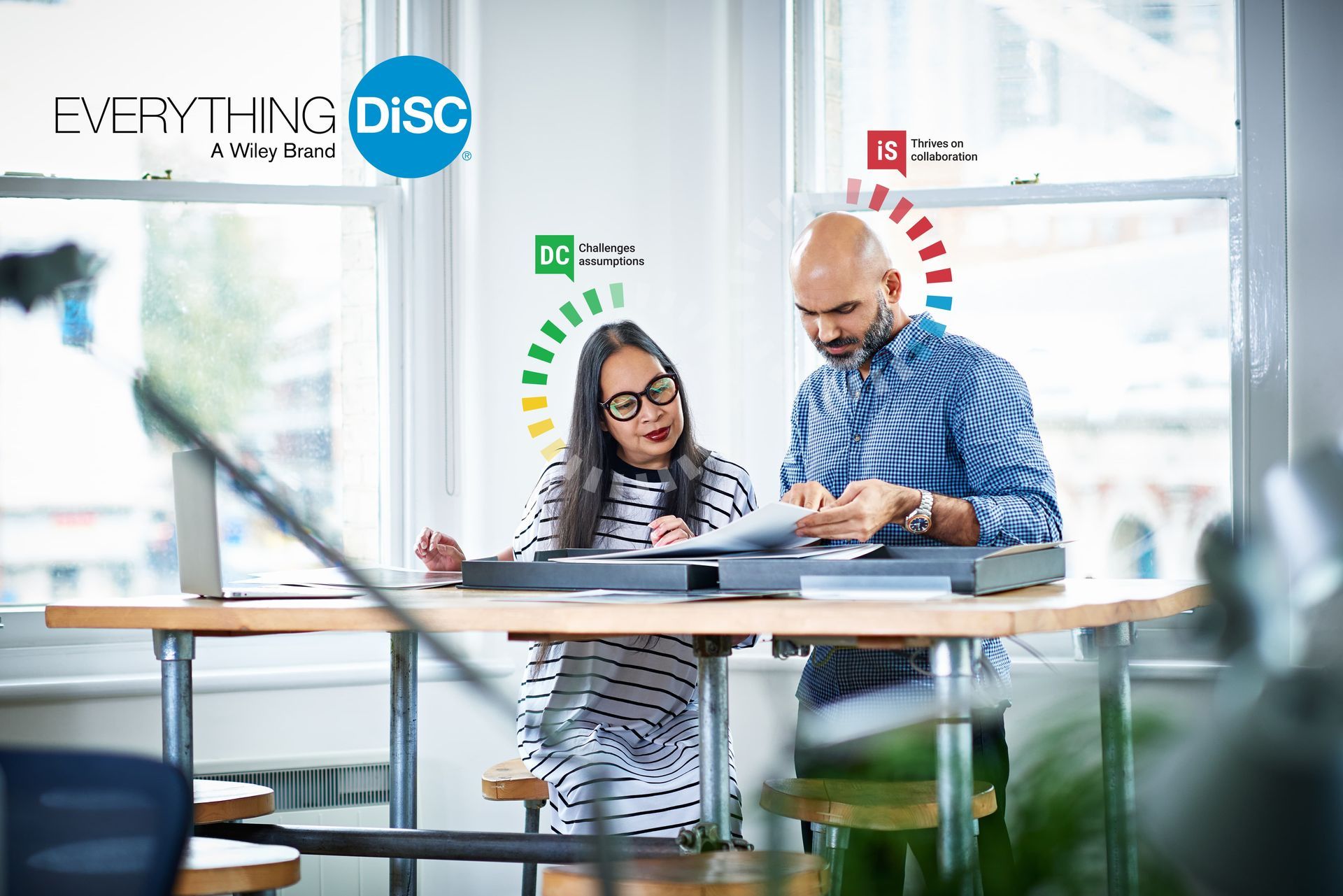 A man and a woman are sitting at a table looking at a laptop.