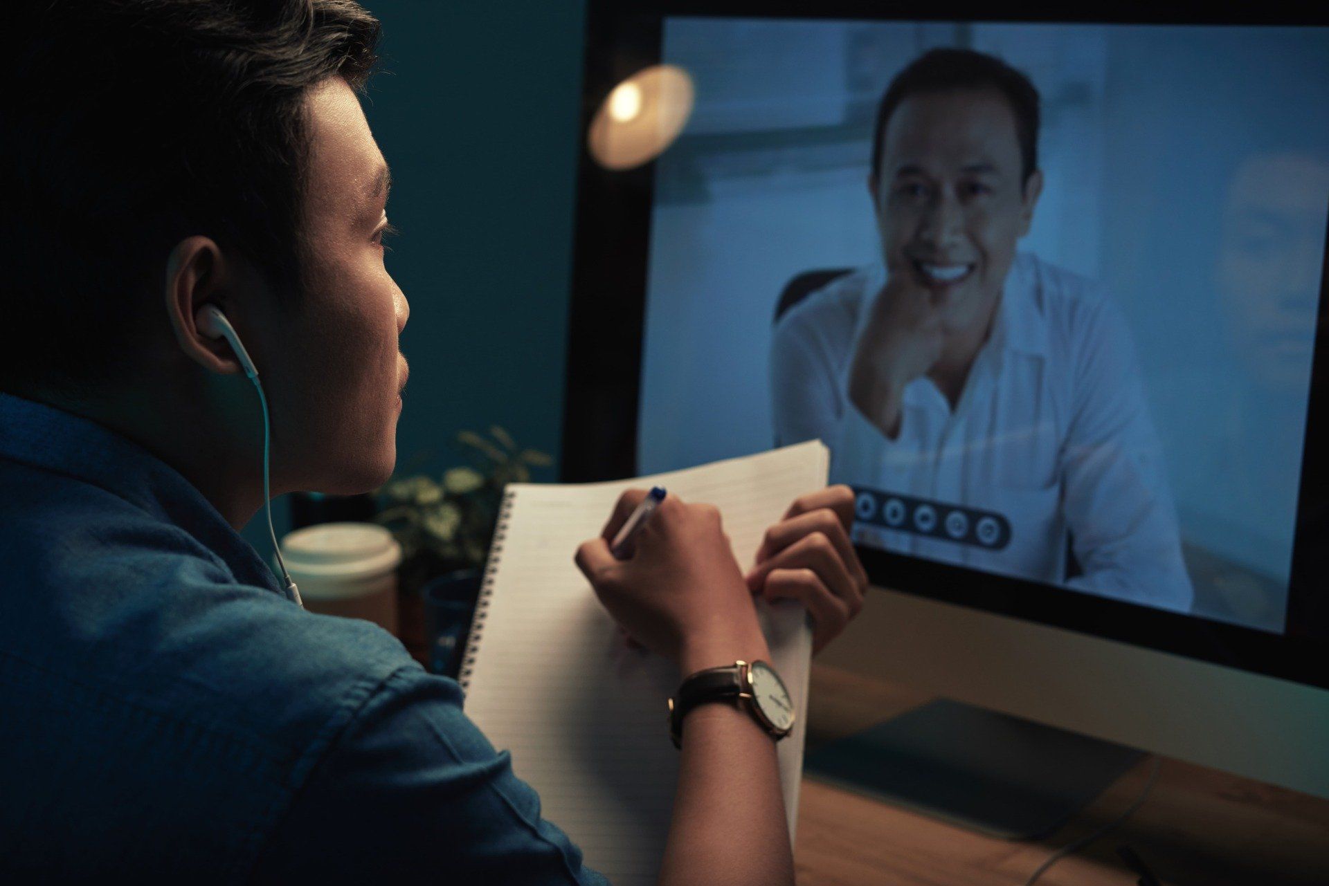 A man is sitting in front of a computer talking to another man.