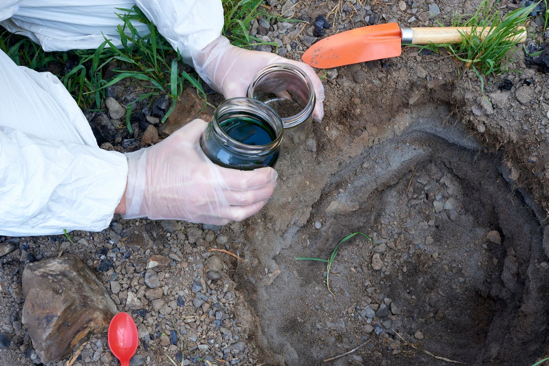 A person is digging in the dirt and holding a jar of liquid A person is digging in the dirt and holding a jar of liquid