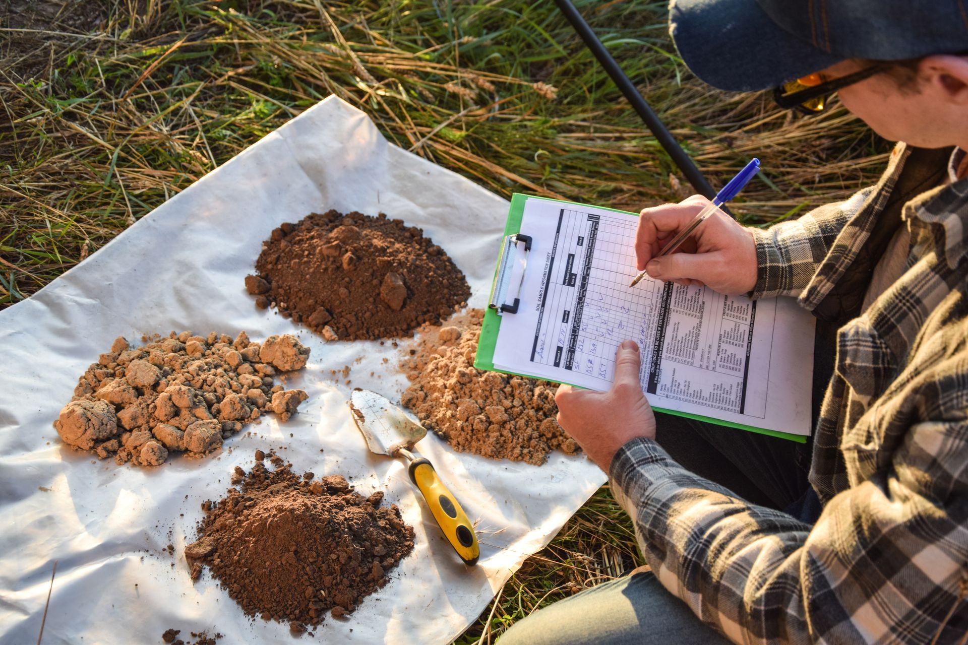 A male agronomist preparing four soil samples for laboratory analysis and writing notes.