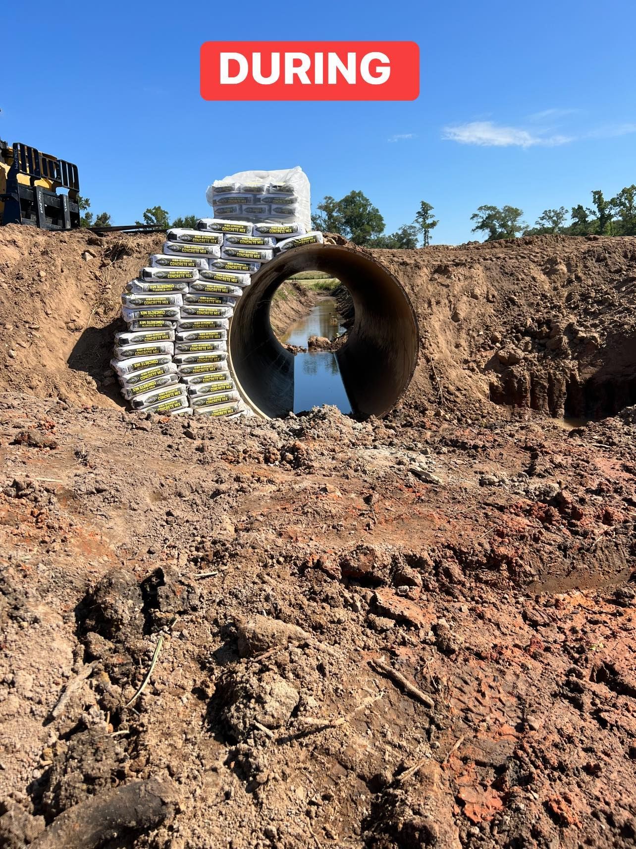 Construction site, tunnel under a mound of soil, bags of plants, blue sky.