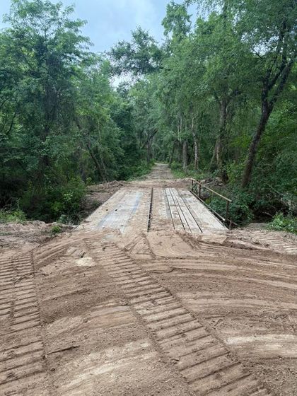 Dirt road with a wooden bridge in a wooded area.