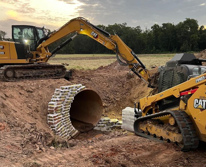 A Caterpillar excavator and skid steer working on a construction site with a large culvert.