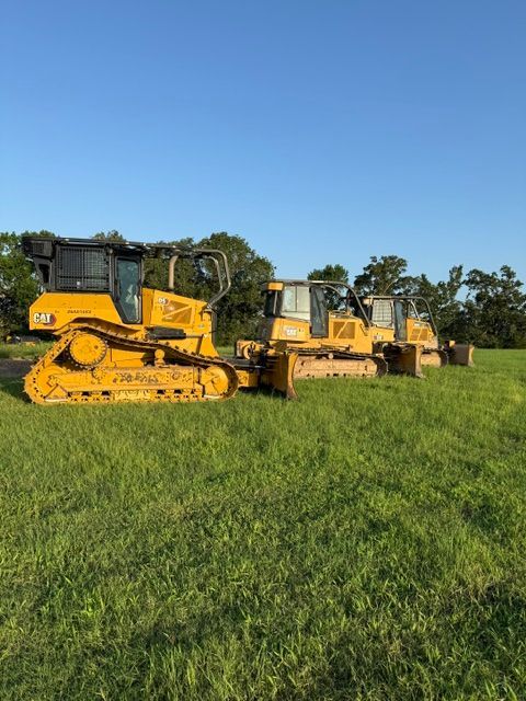 Four yellow bulldozers parked on a grassy field under a blue sky.