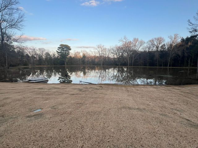 A flooded field with a reflective pond surrounded by trees under a blue sky.