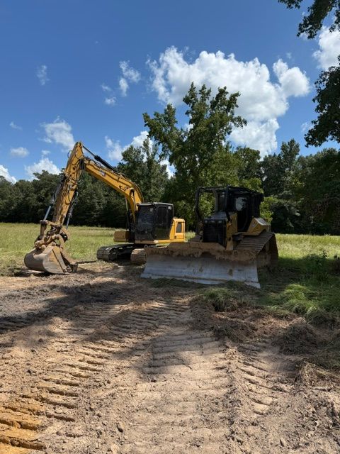 An excavator and bulldozer on a dirt path in a grassy field on a sunny day.