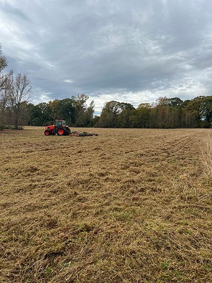 Orange tractor cutting hay in a field under an overcast sky.