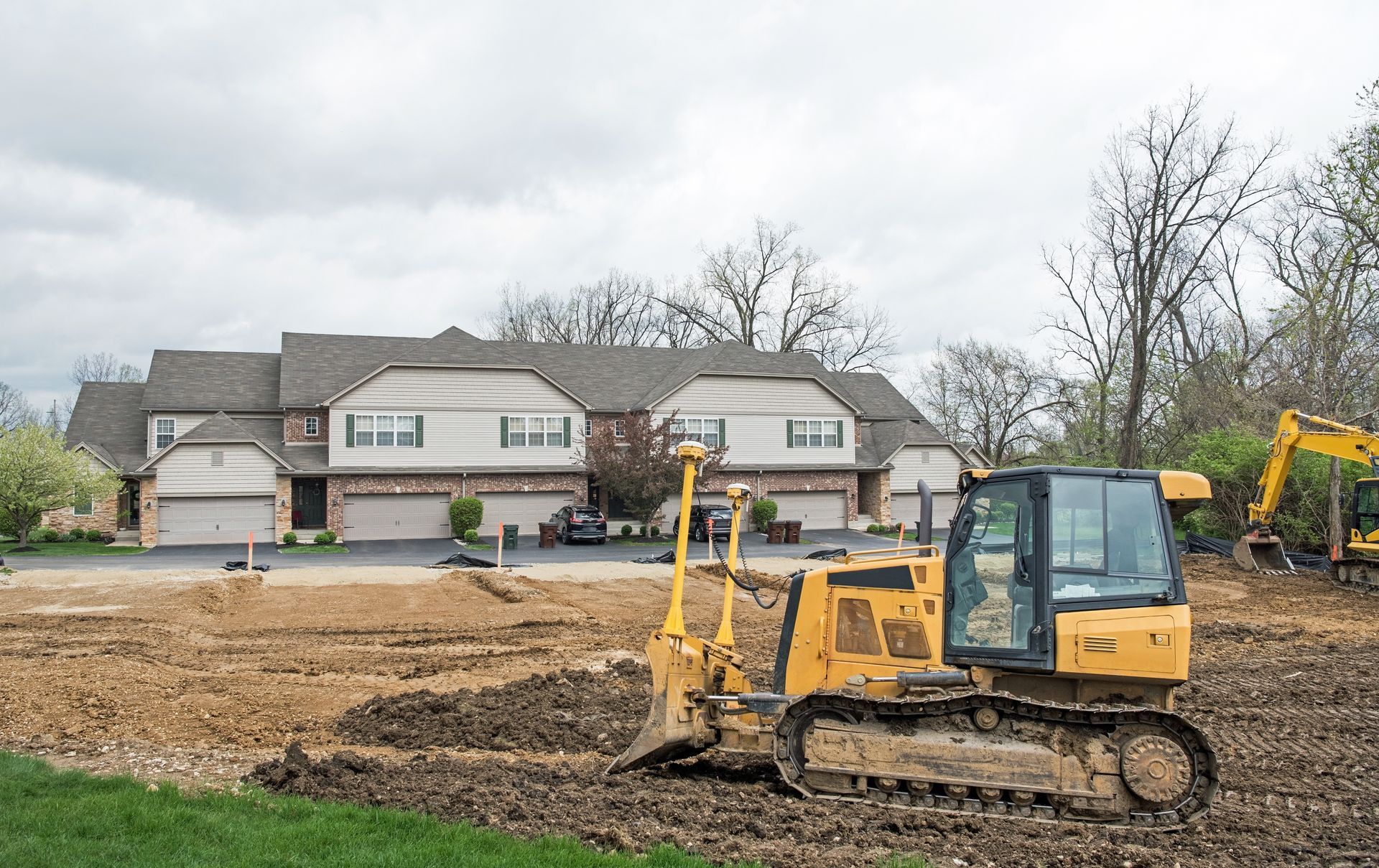 Yellow bulldozer on a construction site leveling brown earth with townhouses in the background.