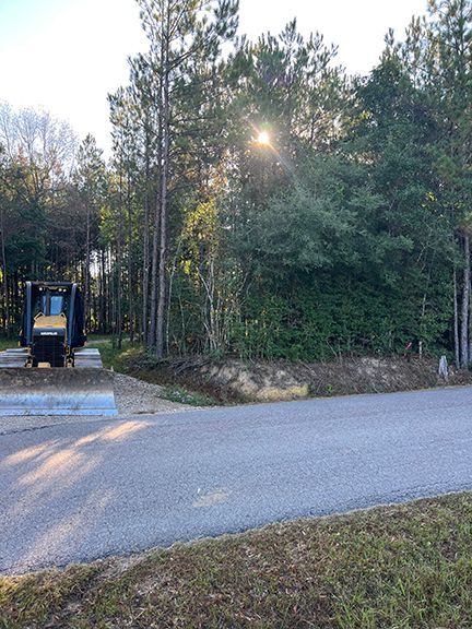 A sunny road corner with trees, a construction vehicle, and a clearing.