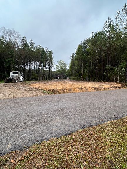 Cleared land next to a road, flanked by trees, with a parked truck. Overcast day.