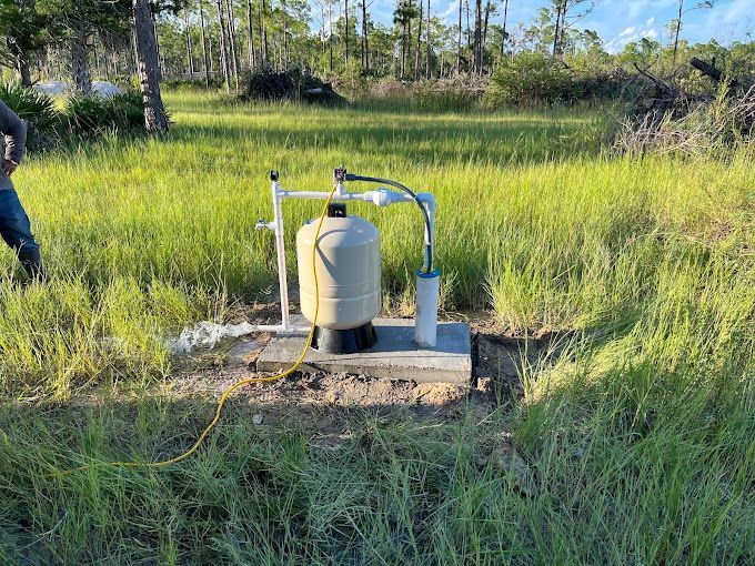 A water pump is sitting in the middle of a grassy field.