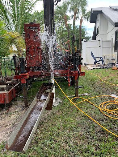 A water well is being drilled in the grass in front of a house.