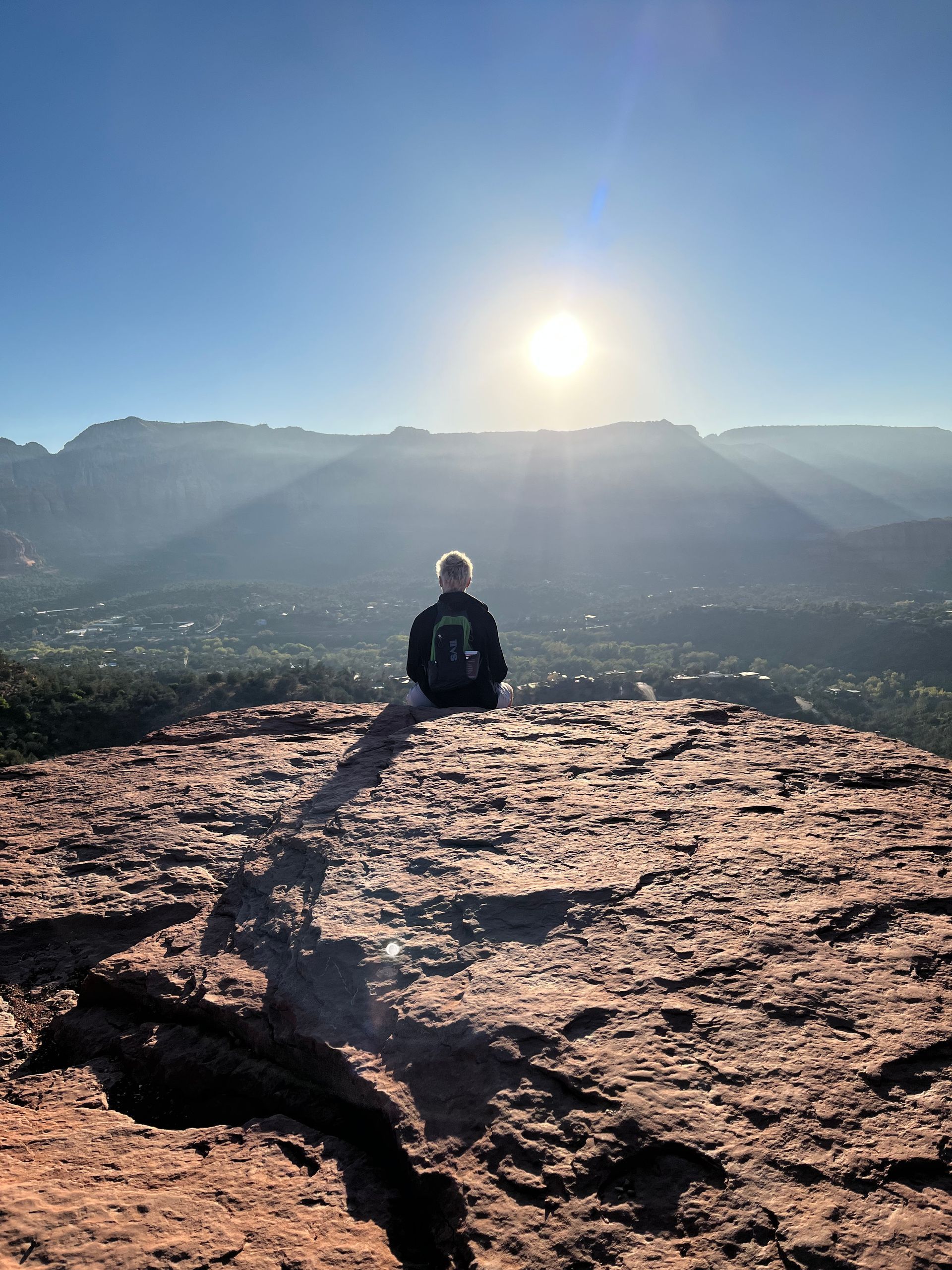 Une personne est assise sur un rocher rouge, surplombant la vallée au lever du soleil.