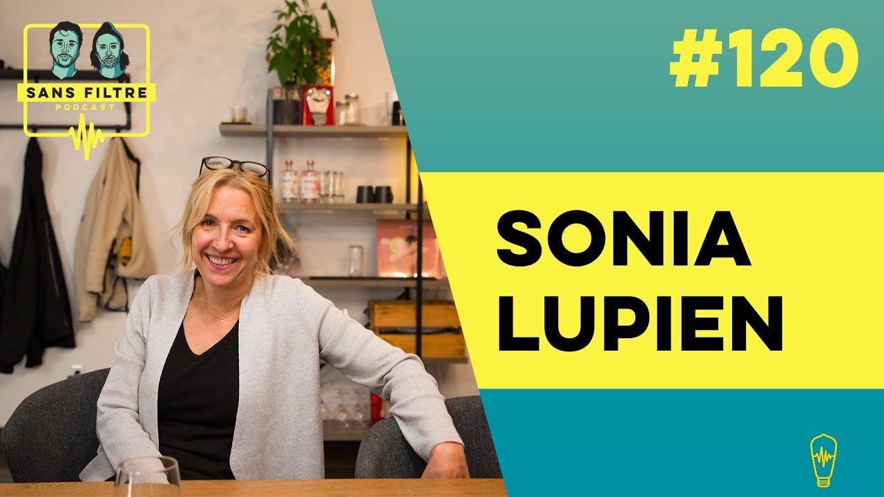 Une femme nommée Sonia Lupien est assise à une table. En arrière-plan, on aperçoit des étagères et un motif graphique vert et jaune avec du texte.
