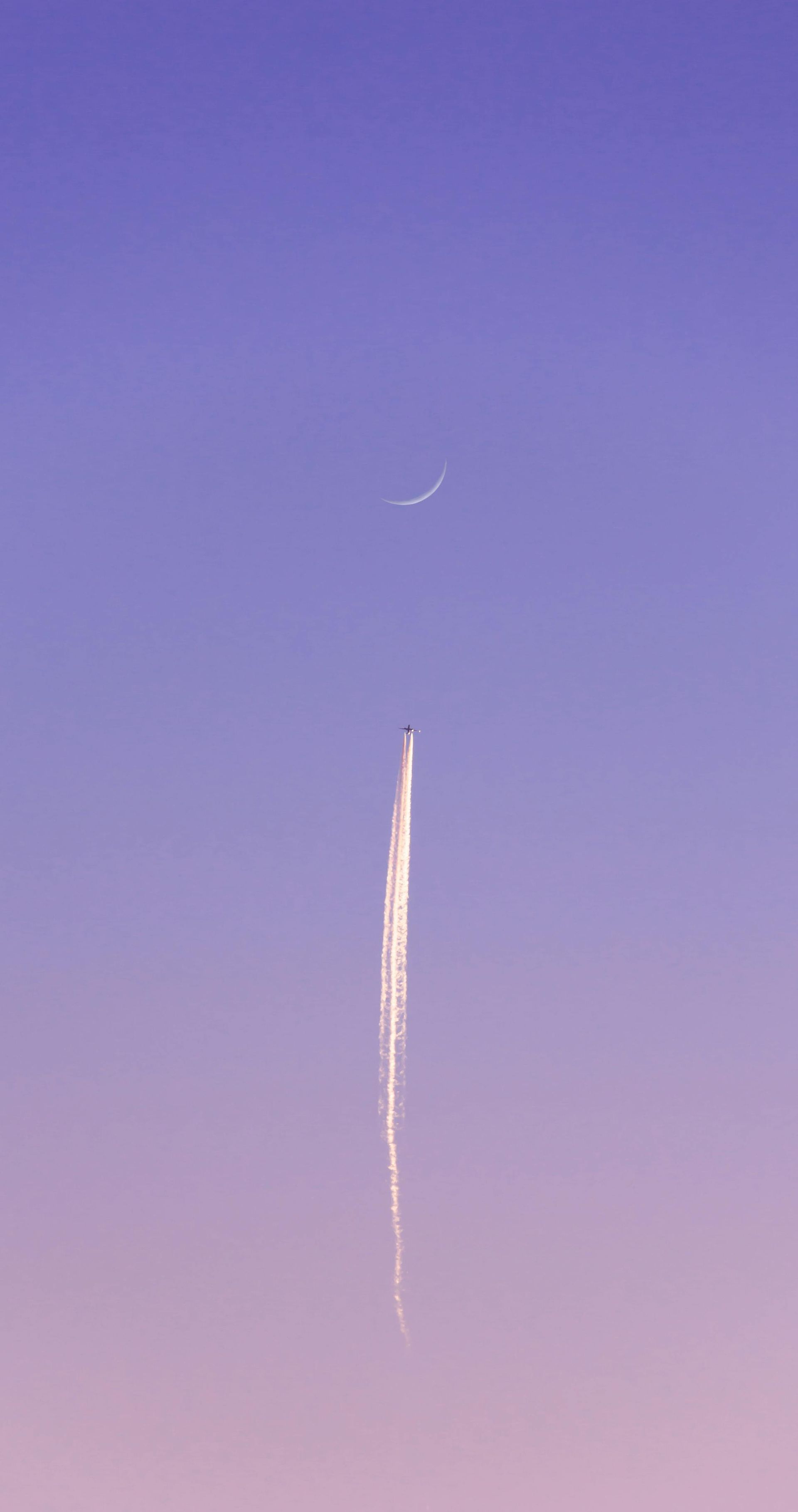 Ciel bleu et violet avec une fine traînée de condensation et un croissant de lune.