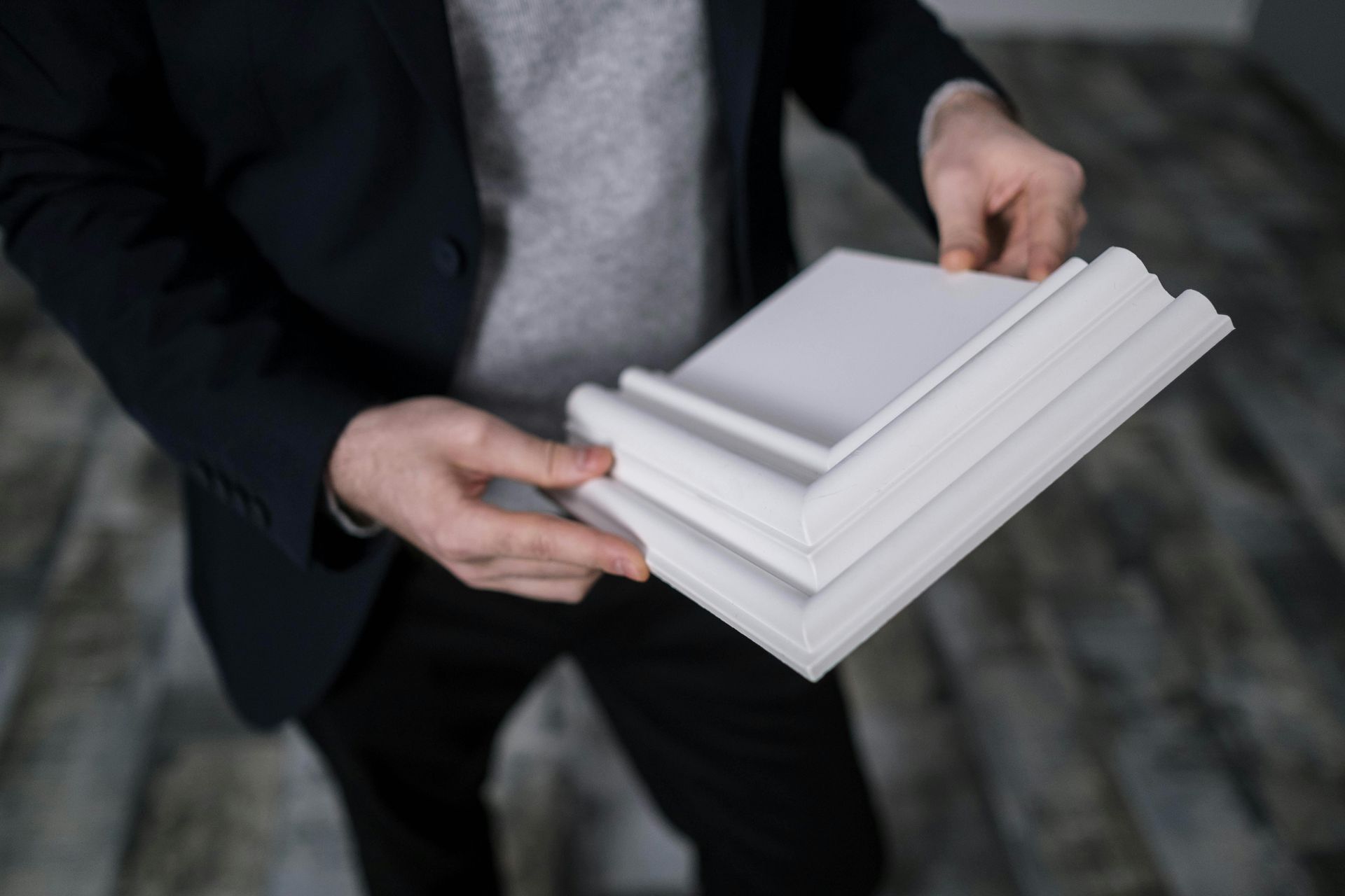 Person in suit holding stack of white architectural molding samples.