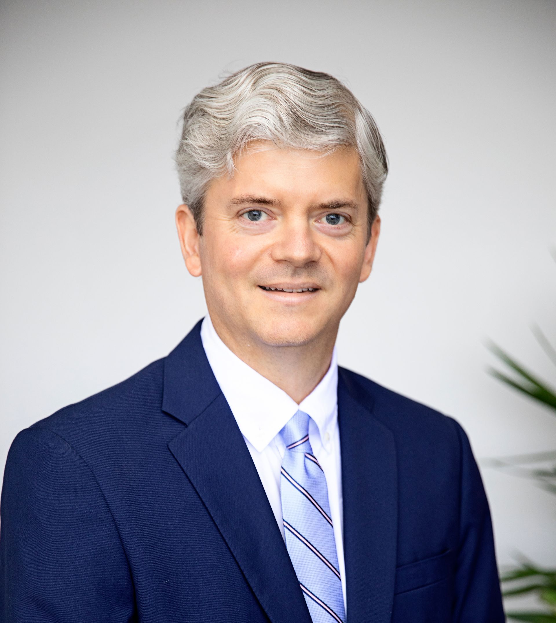 Professional headshot of a Jean Paul LaGarde in a navy suit and striped tie against a light gray background