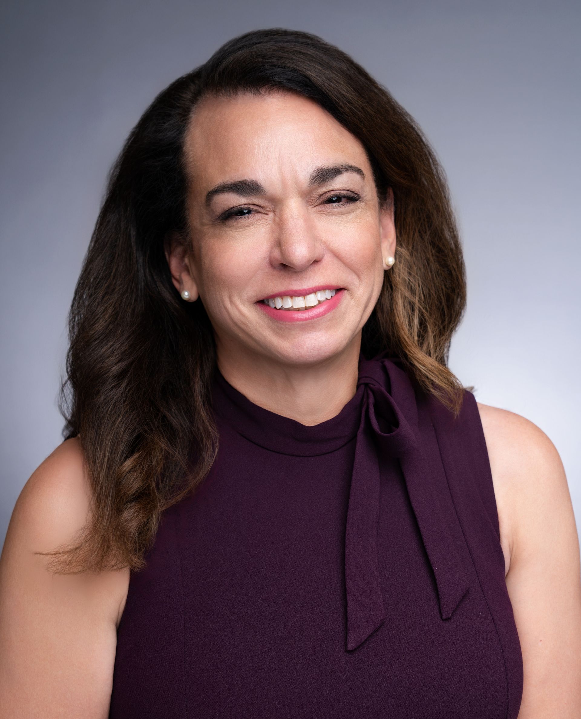 Shana McHaffey smiling in a purple sleeveless top against a gray background