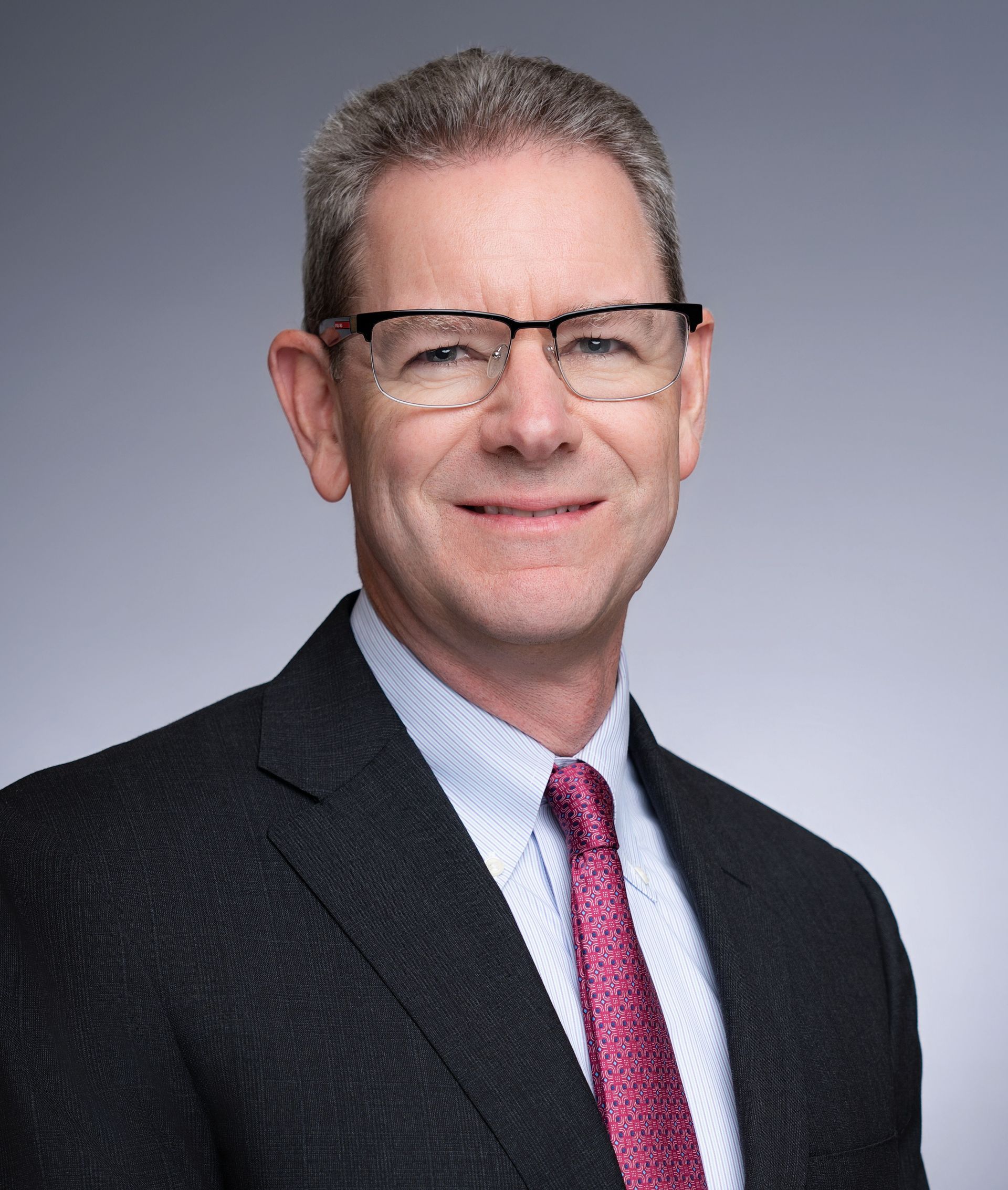 Portrait of Michael Thomas in a dark suit, light blue shirt, and pink tie against a gray background