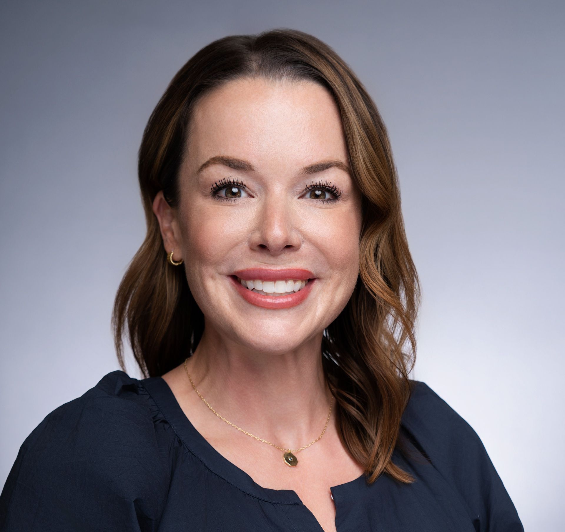 Tamra Gaines smiling in a navy blouse against a gray studio background