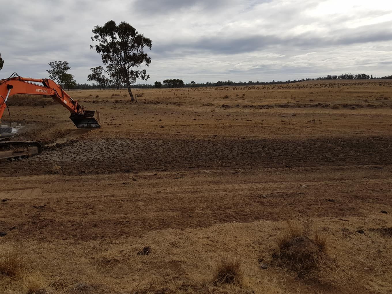 Orange Excavator Working on a Barren Dirt Field Under a Cloudy Sky — Oakleigh Earthmoving in Goondiwindi, QLD