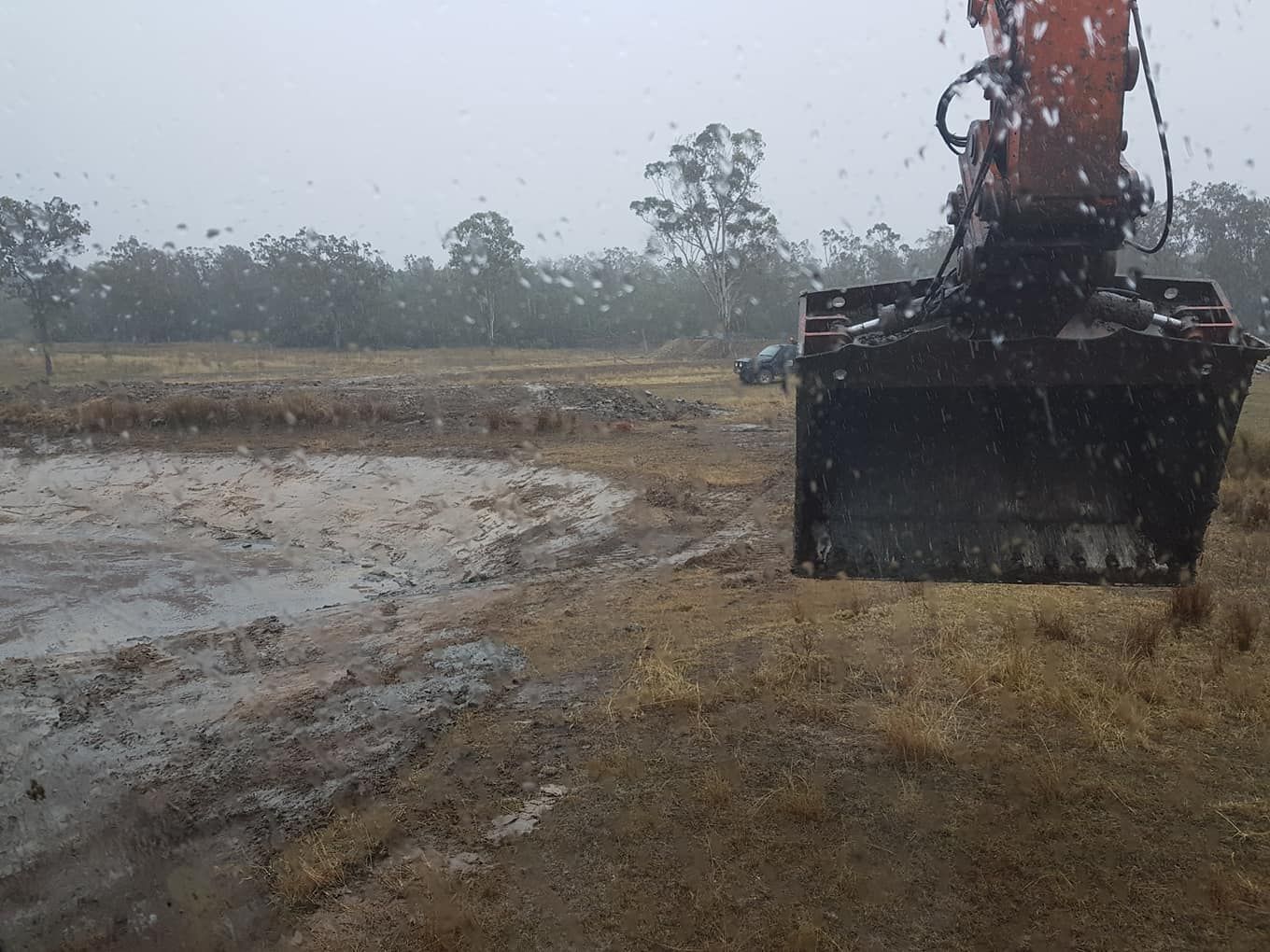 Excavator Bucket at a Muddy Construction Site Under Gray, Rainy Skies — Oakleigh Earthmoving in Toowoomba, QLD