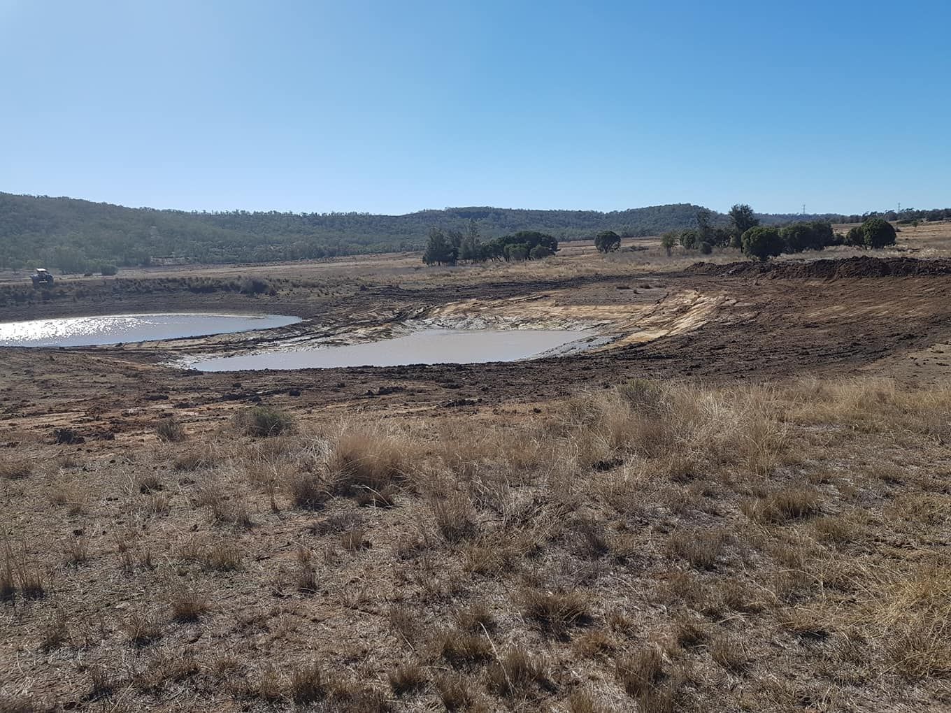 Dry Grassy Marshland With Shallow Water Pools Under a Clear Blue Sky — Oakleigh Earthmoving in Toowoomba, QLD