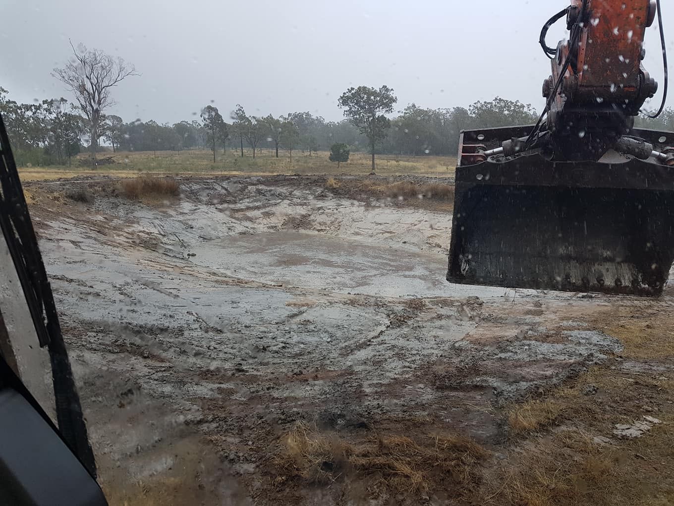Excavator Bucket Scraping Muddy Ground in a Rainy Field — Oakleigh Earthmoving in Kingaroy, QLD