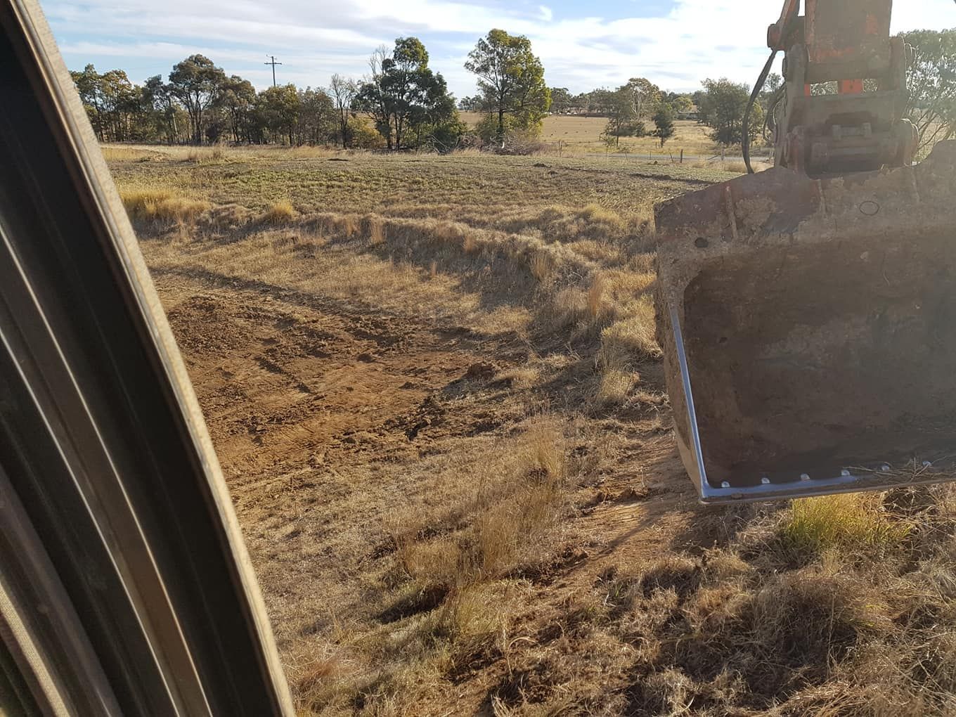 Excavator Bucket Digging Dry Soil in a Grassy Field Under a Clear Sky — Oakleigh Earthmoving in St George, QLD