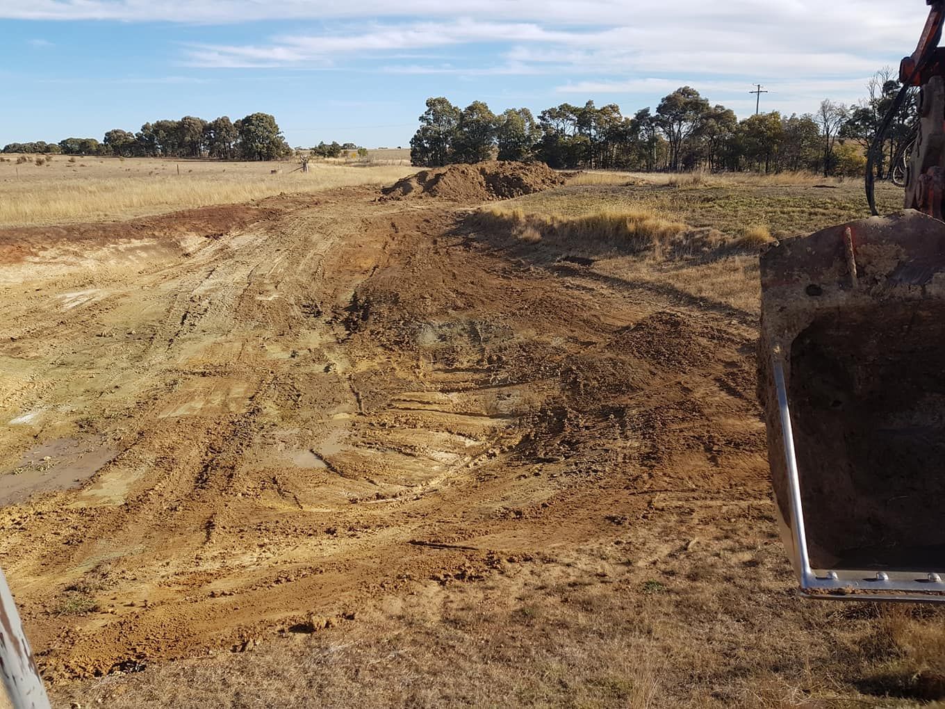 Excavator Grading Dry Dirt in a Rural Field Under a Blue Sky — Oakleigh Earthmoving in Toowoomba, QLD