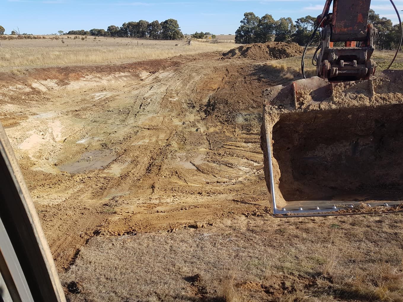 Excavator Digging a Trench in a Dry Field Under Clear Sky — Oakleigh Earthmoving in Toowoomba, QLD