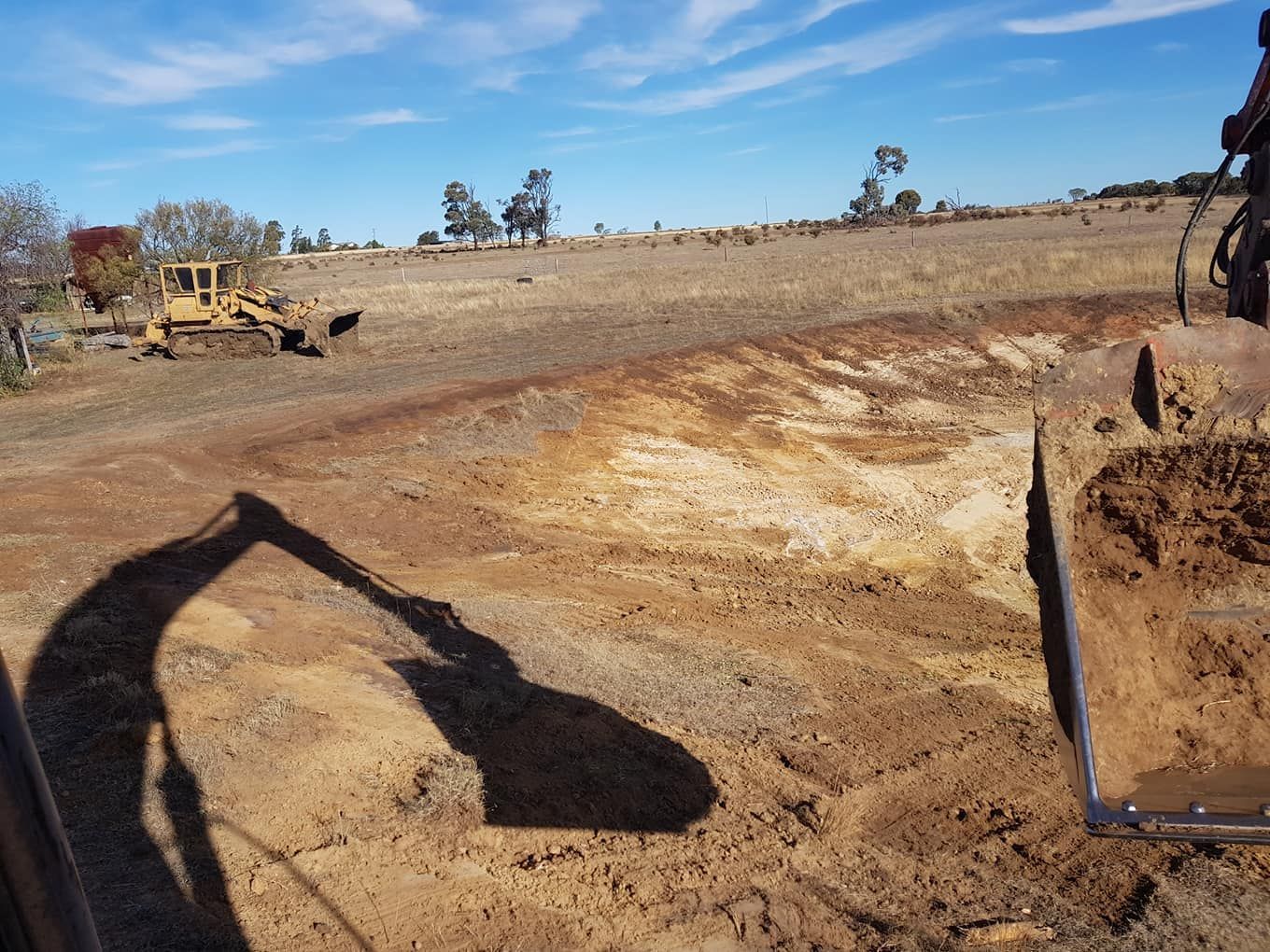 Construction Site With Excavator Shadow Over a Dirt Excavation Under a Blue Sky — Oakleigh Earthmoving in St George, QLD
