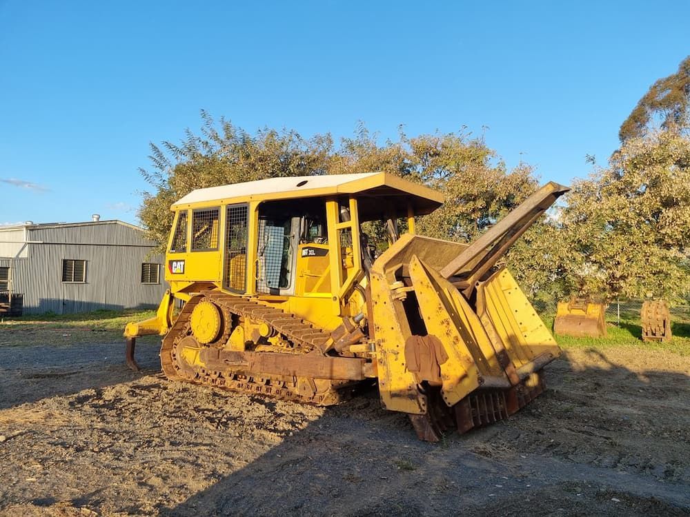 A Yellow Bulldozer is Parked in the Dirt in Front of a House — Oakleigh Earthmoving in Cotswold Hills, QLD