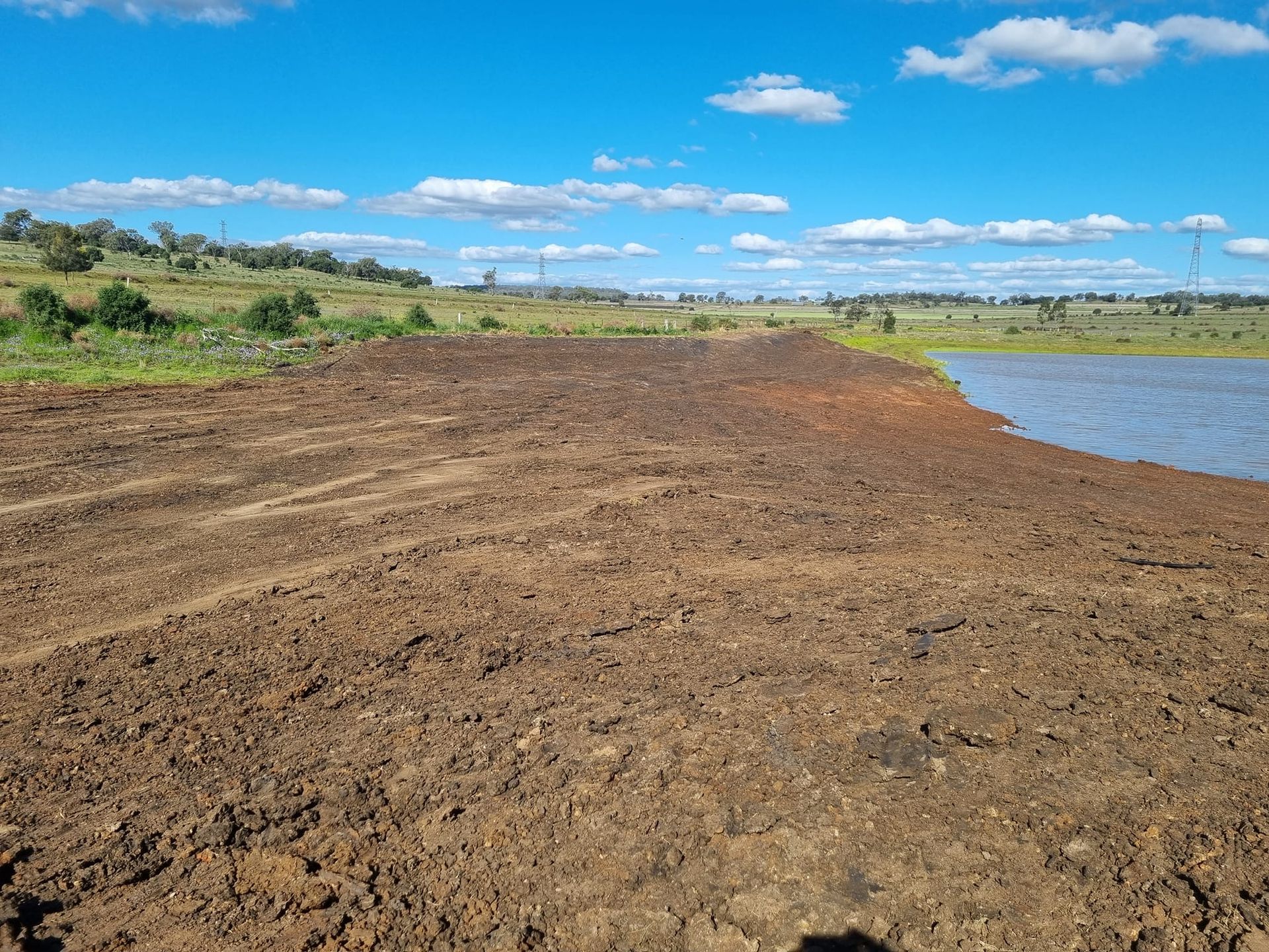 Dirt Shoreline Beside a Calm Lake Under a Blue Sky With Scattered Clouds — Oakleigh Earthmoving in Kingaroy, QLD