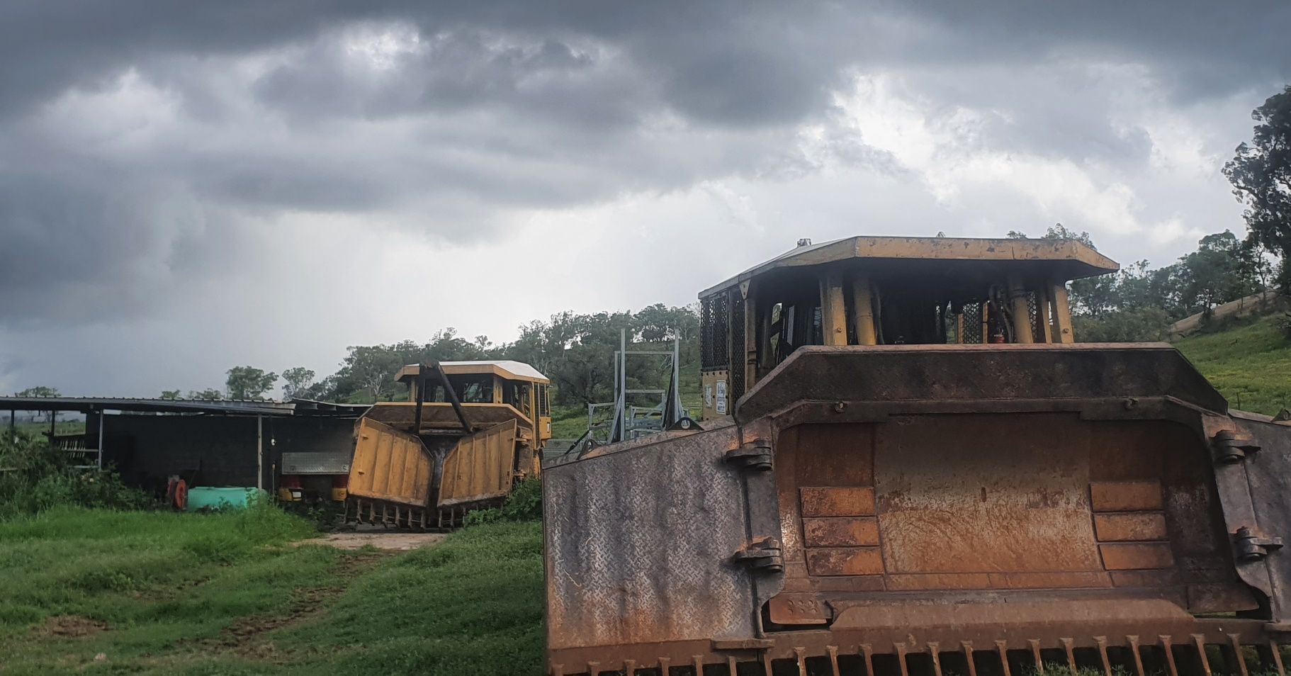 Heavy Machinery on a Grassy Site Under Dark Storm Clouds, With a Large Dump Truck — Oakleigh Earthmoving in Warwick, QLD