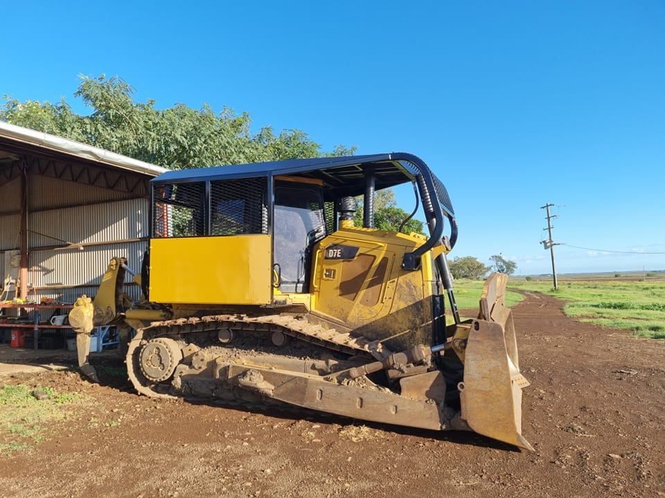 Yellow Bulldozer Parked on a Dirt Field Beside a Shed Under a Blue Sky — Oakleigh Earthmoving in Toowoomba, QLD