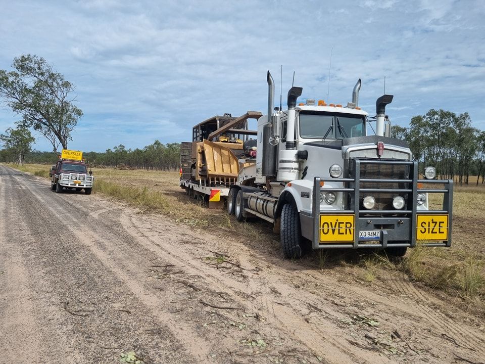 Heavy Hauling Truck With Oversize Signs Towing Machinery on a Dirt Road — Oakleigh Earthmoving in Kingaroy, QLD