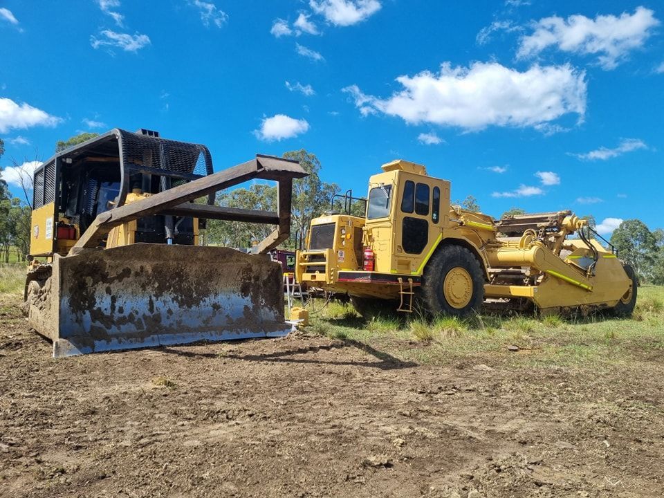 Yellow Bulldozer and Road Grader on a Dirt Field Under a Blue Sky With Clouds — Oakleigh Earthmoving in Warwick, QLD