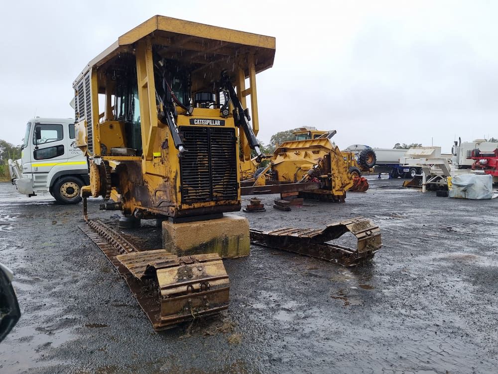 A Yellow Bulldozer is Sitting in a Muddy Parking Lot Next to a Truck — Oakleigh Earthmoving in Cotswold Hills, QLD