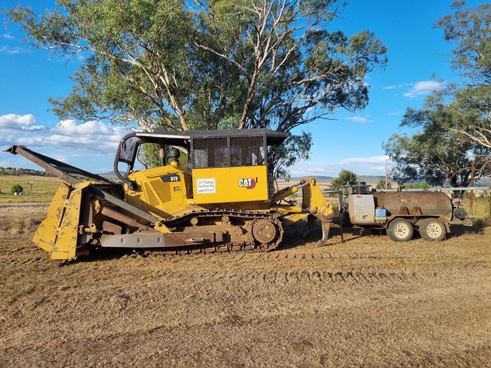 Yellow Bulldozer With Attached Trailer on a Dirt Road in a Rural Field — Oakleigh Earthmoving in Warwick, QLD