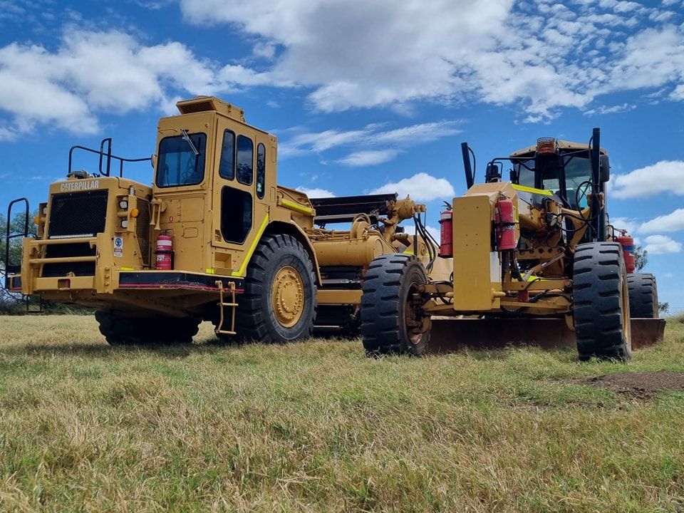 Two Yellow Heavy Tractors on a Grassy Field Under a Blue Sky — Oakleigh Earthmoving in Warwick, QLD