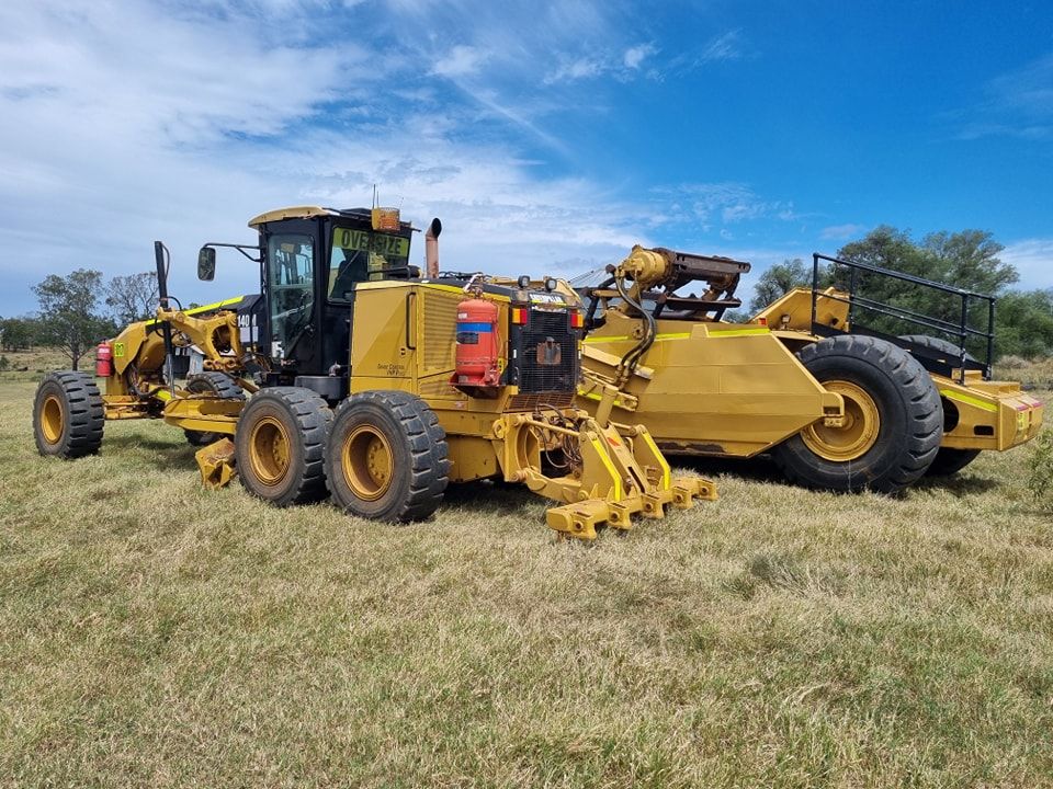 Yellow Road Grader and Heavy Machinery Parked in a Grassy Field — Oakleigh Earthmoving in Cotswold Hills, QLD
