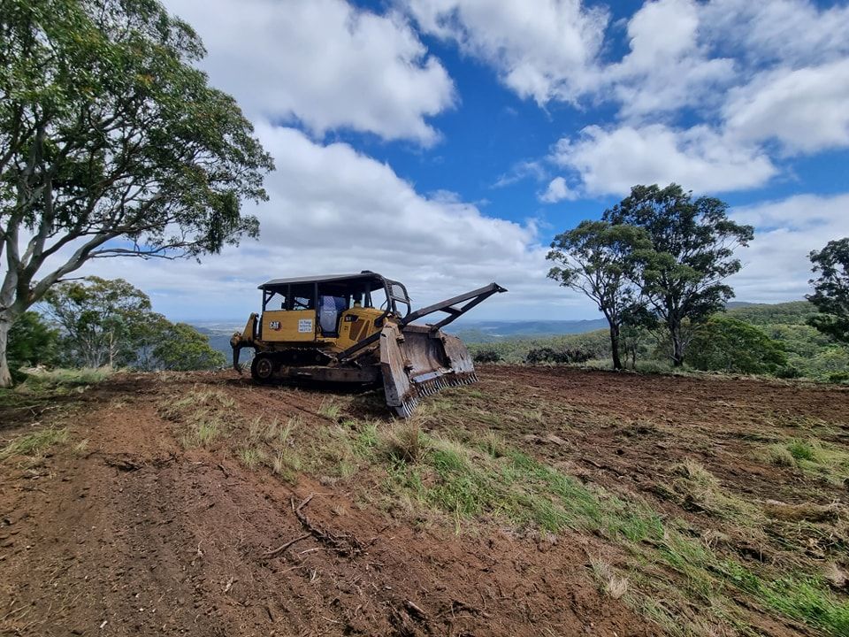 Bulldozer Clearing a Dirt Field Under a Partly Cloudy Sky With Trees and Hills — Oakleigh Earthmoving in Kingaroy, QLD