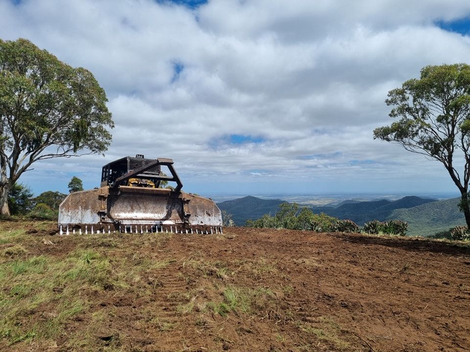 Bulldozer on a Dirt Hilltop With Trees and a Cloudy Mountain Landscape — Oakleigh Earthmoving in Kingaroy, QLD
