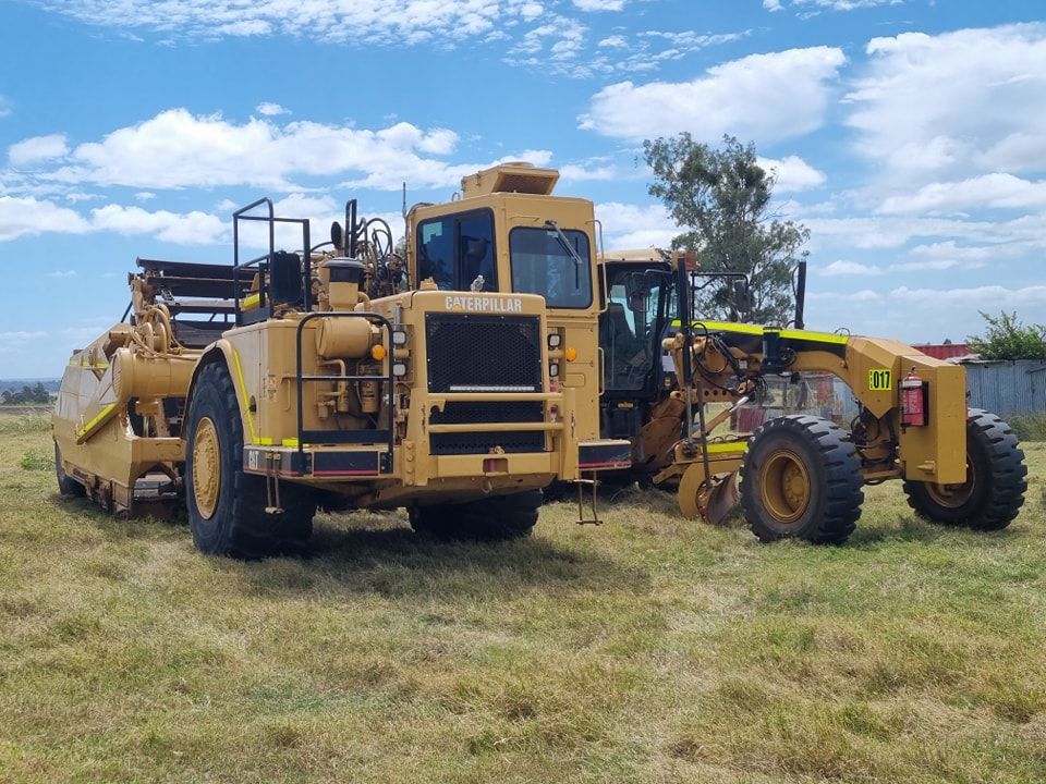Yellow Construction Machinery Parked in a Grassy Field Under a Blue Sky — Oakleigh Earthmoving in Cotswold Hills, QLD