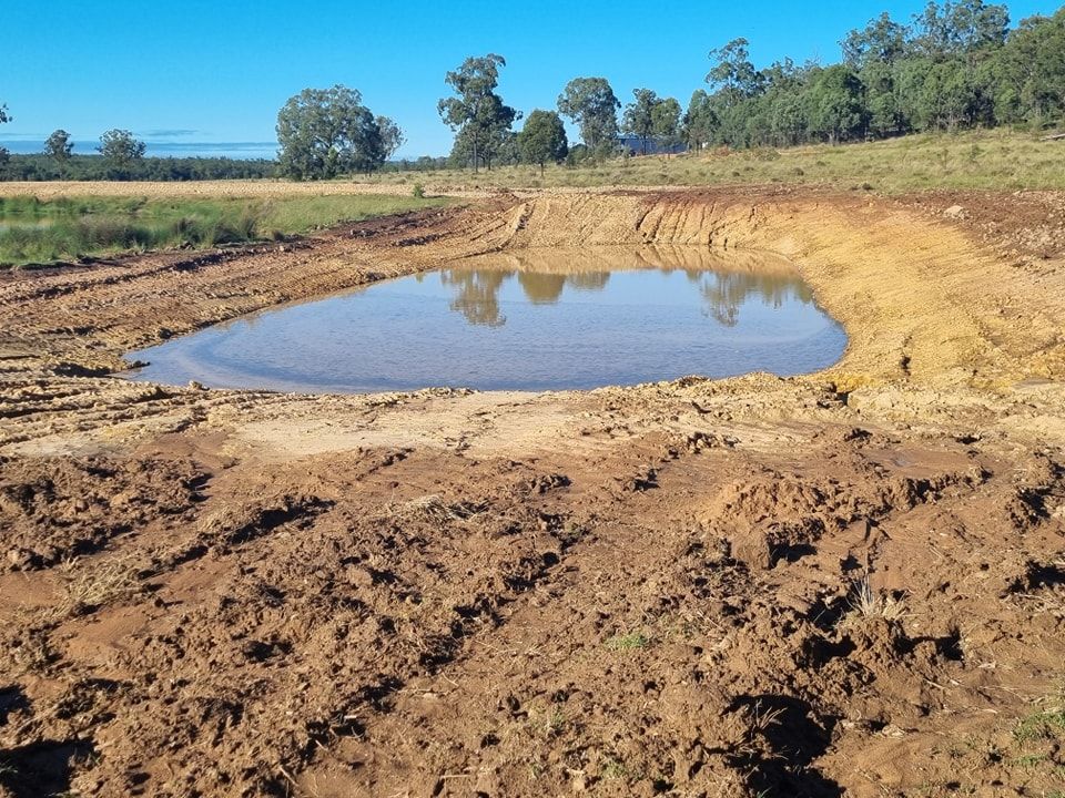 Dry Dirt Pit With a Small Muddy Water Pool in a Rural Landscape Under a Clear Blue Sky — Oakleigh Earthmoving in Warwick, QLD
