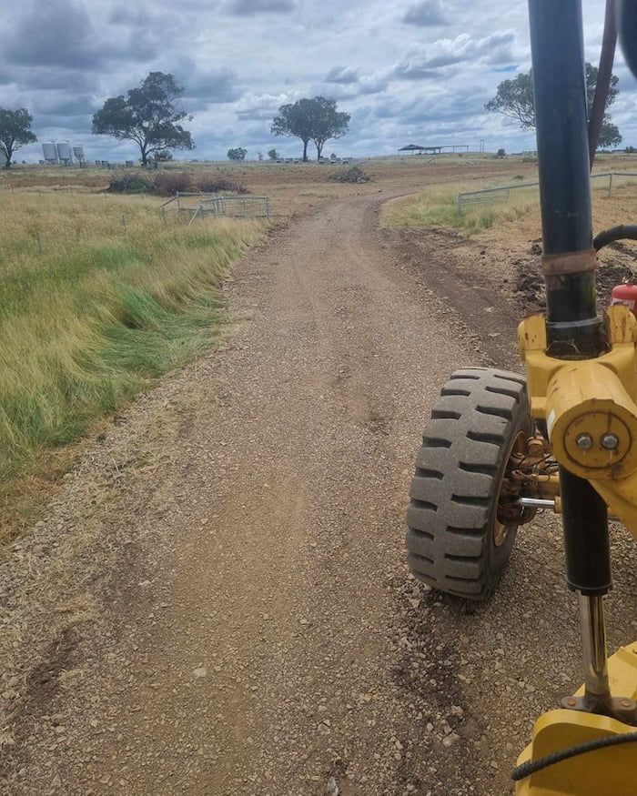 A Yellow Tractor is Driving Down a Dirt Road — Oakleigh Earthmoving in Cotswold Hills, QLD