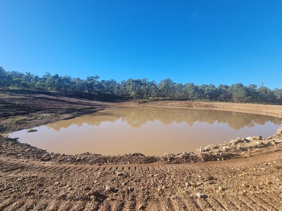 Muddy Construction Pond Under a Clear Blue Sky, With Trees in the Background — Oakleigh Earthmoving in Warwick, QLD