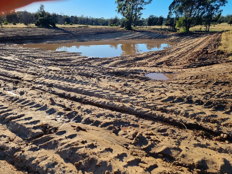 Sandy Dirt Road With Tire Tracks and Puddles in a Sunny Rural Landscape — Oakleigh Earthmoving in Warwick, QLD