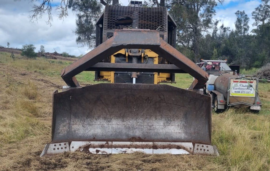 Bulldozer Front Blade in a Grassy Field With Workers and a Utility Truck Nearby — Oakleigh Earthmoving in Cotswold Hills, QLD